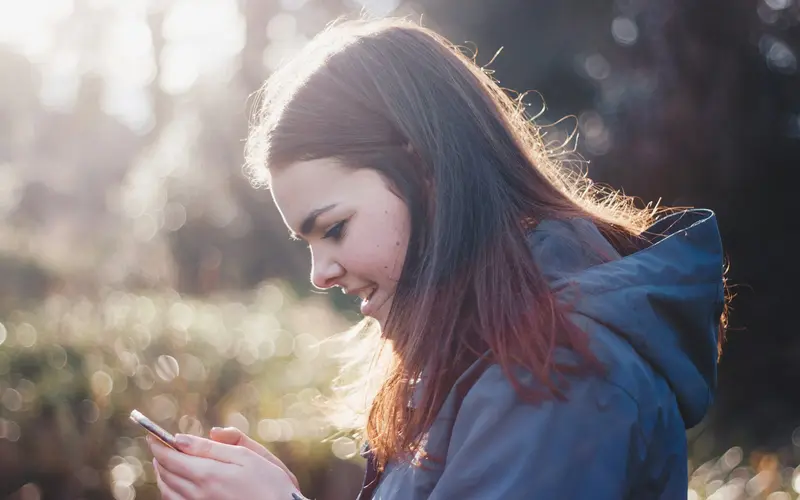 Een jonge vrouw kijkt glimlachend op haar telefoon